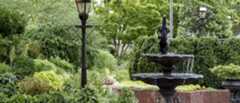 Cast iron three-tiered fountain with bird motif framed by raised brick beds planted with varying shades of green
