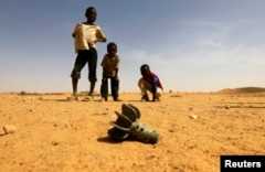 FILE - Children look at the fin of a mortar projectile that was found at the Al-Abassi camp for internally displaced persons, after an attack by rebels, in Mellit town, North Darfur, March 25, 2014.