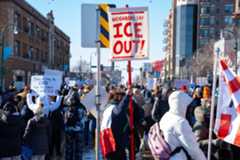 People protesting in Minneapolis, including someone with a sign that says "Neighbors say ICE out!" Another sign held in the background reads "Minnesota may be cold but we don't fuck with ICE"