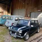 Three classic cars parked in a row in front of a brown wooden barn