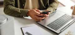 image of a man on his phone in front of an open laptop