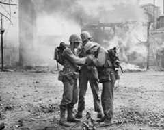 a couple of soldiers smoking in front of a burning building