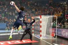 two men are playing soccer in front of an arena full of people, with one man jumping up to catch the ball