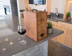 a wooden box sitting on top of a kitchen counter next to a glass of wine