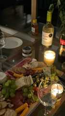 a glass table topped with lots of different types of cheese and meats next to bottles of wine