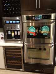 two stainless steel ovens with ketchup and wine bottles on the front, in a kitchen