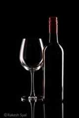 a wine glass next to a bottle on a black surface with reflection in the water