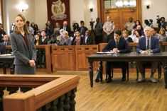 a woman standing in front of a group of people sitting at desks with microphones