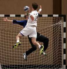 two young men playing soccer in front of a goal net with the ball coming towards them
