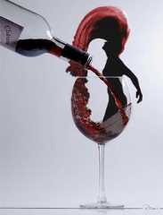 a wine glass filled with red liquid being poured into it and a silhouette of a woman in the background