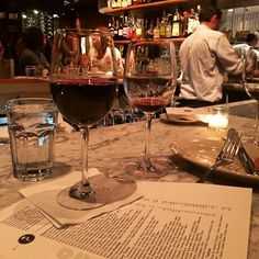 two glasses of red wine sitting on top of a table next to papers and bottles