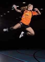a woman jumping in the air with a soccer ball on her feet and wearing an orange shirt