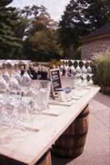 wine glasses and bottles are lined up on an outdoor table with a chalkboard sign