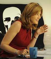 a woman sitting at a desk with her hands out to the side, and talking