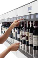 two hands reaching for a wine glass in front of a row of bottles on a shelf