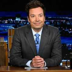 a man in a suit and tie sitting at a desk with his hands folded up