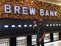 a man standing in front of a sign that says brew bank with lights on it