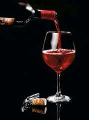 red wine being poured into a glass in front of a bottle and corkscrew
