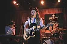a woman singing into a microphone while holding a guitar in front of two other people