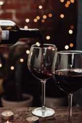 a person pouring wine into two glasses on a table with lights in the back ground