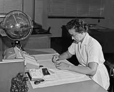 a woman sitting at a desk writing on a piece of paper with a globe in the background