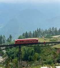 a red train traveling over a bridge in the middle of a lush green forest covered hillside