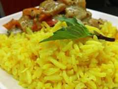 a white plate topped with yellow rice and meat covered in green leafy garnish