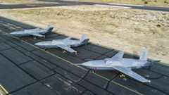 Three General Atomics unmanned aircraft lined up on a runway at a desert airfield, painted in U.S. Air Force markings.