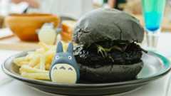 A black burger, on a plate with a small Totoro model, and fries