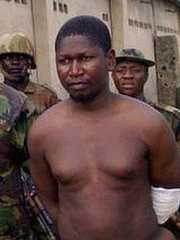 Mohammed Yusuf, bare-chested and with a bandage on his arm, surrounded by soldiers