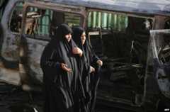 Iraqi women pass a car destroyed in a bombing in Baghdad, 18 June