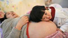 A woman, pregnant with her second child, lies on a bed as her daughter places her head on her mother's stomach in Hefei, Anhui province, China, in February 2014