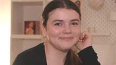 Martha, with her hair tied up and wearing a black top, smiles and looks into the camera