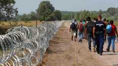 A policeman escorts migrants on the Hungarian-Serbian border in Asotthalom, Hungary on 13 August 2015