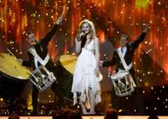 Eine Sängerin mit Mikrofon steht barfuß auf der Bühne, begleitet von zwei Schlagzeugern.