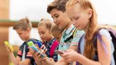Eine Gruppe von Schulkindern sitzt nebeneinander und benutzt Smartphones.