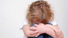 Ein trauriges Kind mit blonden Locken versteckt sein Gesicht in den Armen.