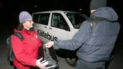 Eine Frau in roter Jacke übergibt einem Mann eine Schlaftüte vor einem „Kältebus“.