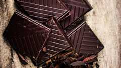 Mehrere Stücke dunkler Schokolade liegen auf einem Holztisch.