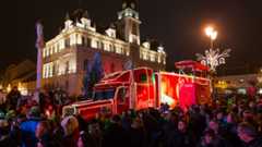 Ein beleuchteter Coca-Cola-Truck steht vor dem Rathaus auf einem belebten Platz.