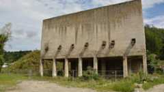 Ein großes, verlassenes Betongebäude mit mehreren Öffnungen steht auf einem Feld.