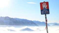 Ein Lawinengefahr-Schild steht vor einer verschneiten Berglandschaft.