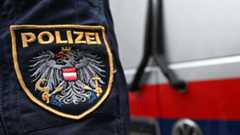 Ein Polizist mit österreichischem Wappen steht vor einem Einsatzfahrzeug mit rotem und blauem Streifen.