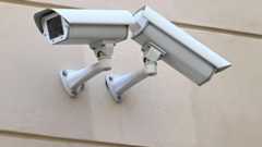 Zwei weiße Überwachungskameras sind an einer Wand montiert.