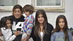 Eine Mutter mit ihren vier Kindern steht vor einer weißen Hauswand.