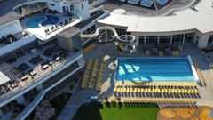 Großer Außenpool mit vielen gelben Liegestühlen, Wasserrutsche, Sonnenterrassen und einem runden Whirlpool auf dem Dach.