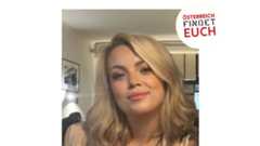 Junge Frau mit schulterlangem blondem Haar und beigem Blazer sitzt in einem Raum und lächelt leicht.