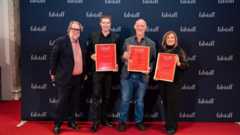 Vier Personen stehen auf rotem Teppich vor einer Wand mit „falstaff“-Schriftzug und halten gerahmte Auszeichnungen.