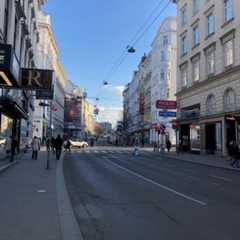 Blick auf eine belebte Straße in Wien mit Geschäften und Passanten.
