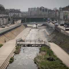 Der Wienfluss fließt kanalisiert durch Wien, flankiert von Straßen und Gehwegen.